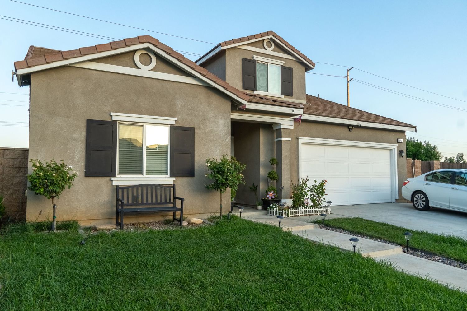 Two-story beige stucco suburban home with white garage door and green front lawn.