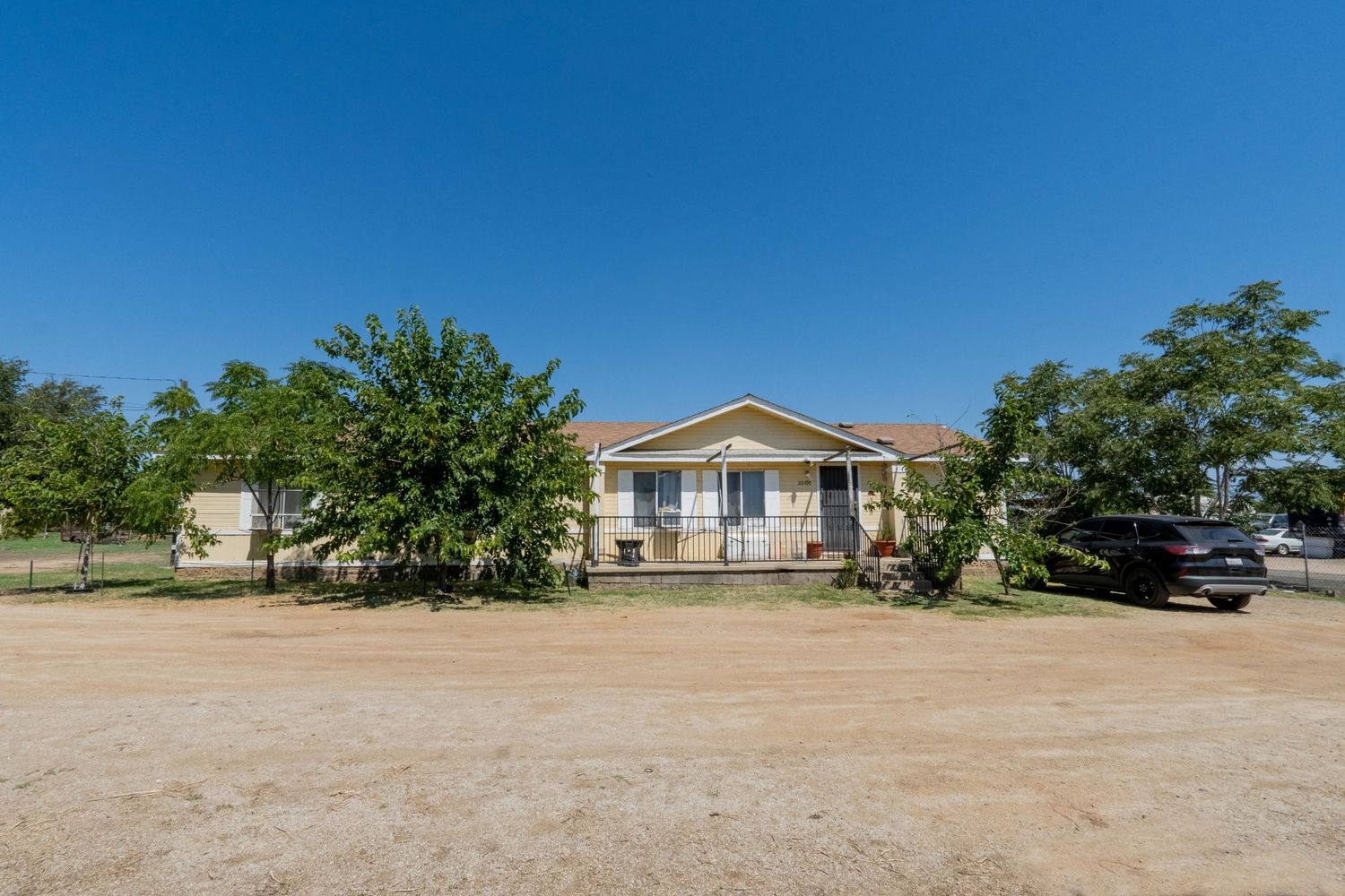 Single-story ranch home with a covered porch surrounded by mature trees on a spacious dirt lot.