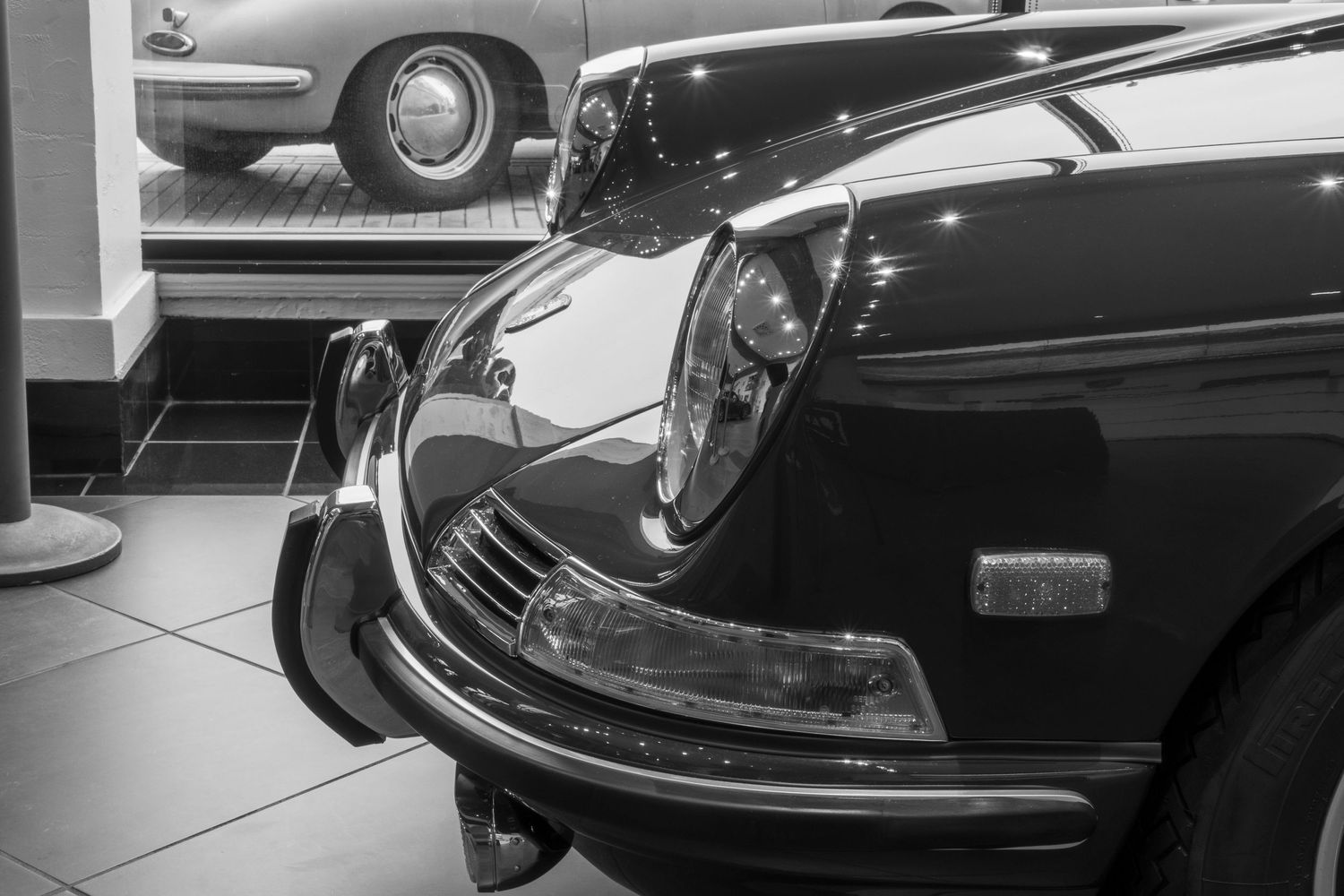 Black and white close-up of a vintage Porsche 911 front end in a showroom.