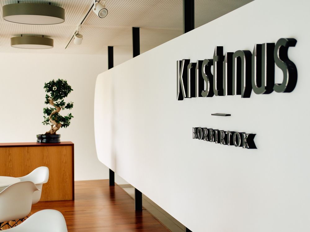 Modern white wall with Kristinus logo in black lettering and minimalist interior design.