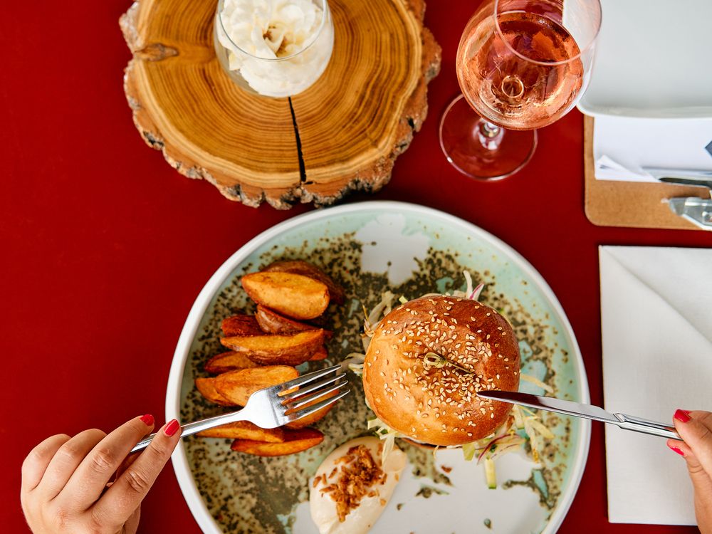 Overhead view of a gourmet burger and roasted carrots on a plate with a glass of rosé wine and wooden platter.