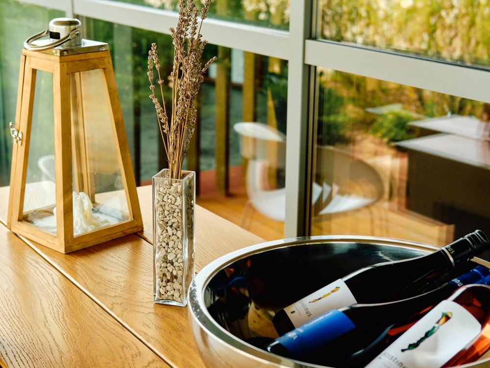Wine bottles in ice bucket with decorative gold lantern and dried flowers on wooden table.
