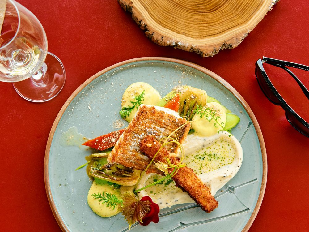 Elegantly plated salmon dish with green garnishes on a blue ceramic plate.
