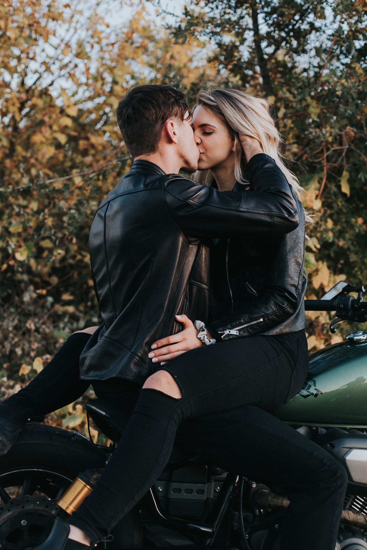 Intimate moment shared on motorcycle with fall foliage background.