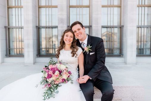 A wedding couple sitting together in front of elegant white columns on their special day at Draper Temple.