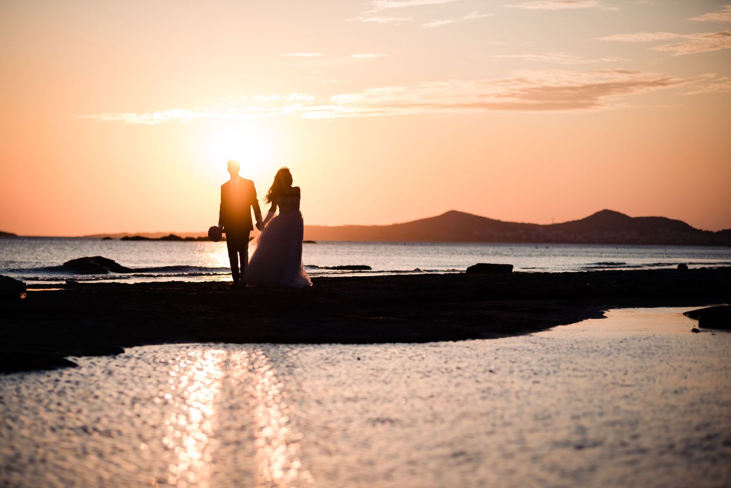 Wedding in Sounio, Greece. A beautiful couple, smiling at each other on a sandy beach as the sun sets in the background.