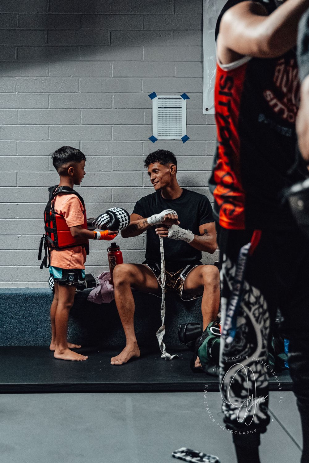 Martial artists preparing for training while seated along a gym wall.