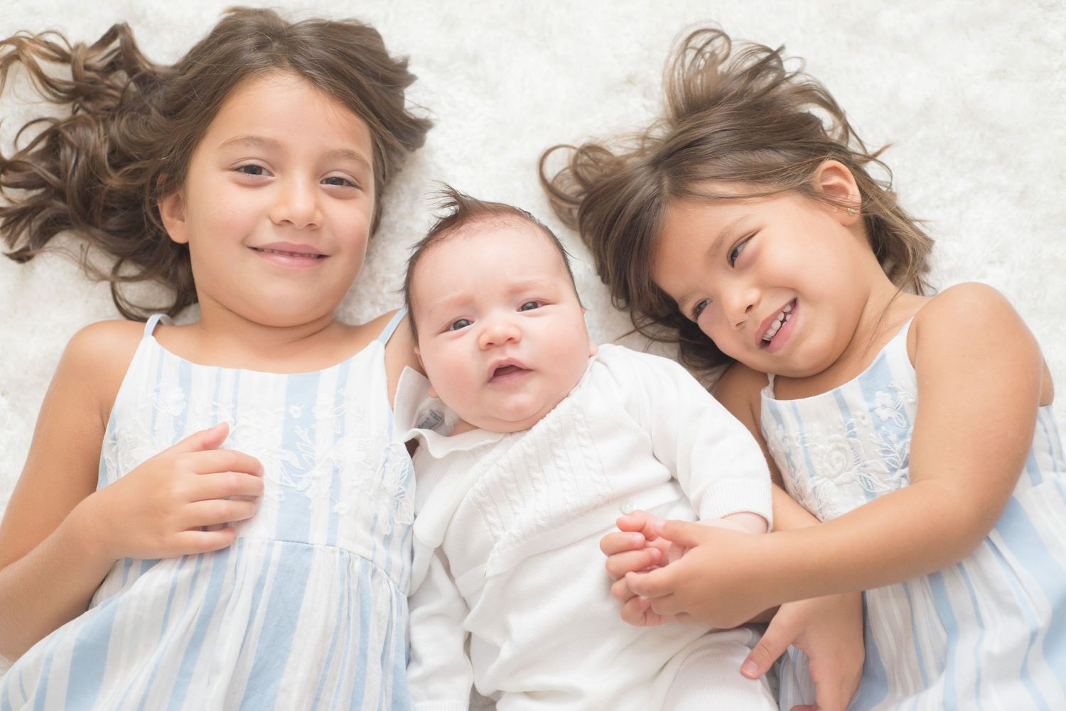 two sisters and baby brother lying on their back looking up during a lifestyle session