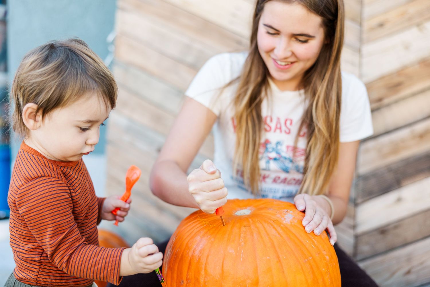 Parent and child working together to clean out a large orange pumpkin.