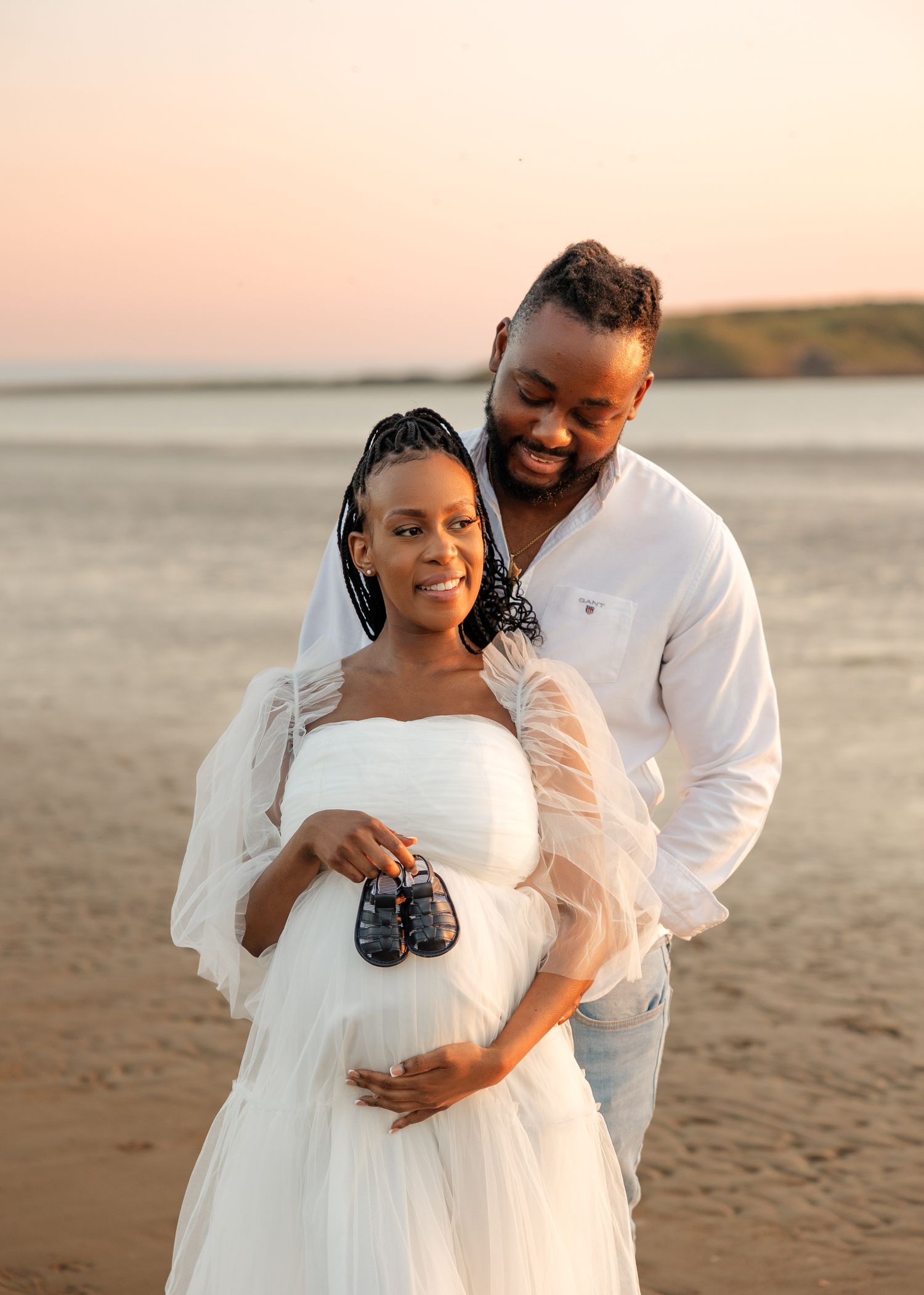 Expectant couple holding baby shoes during sunset beach maternity photoshoot in Adelaide, Australia.