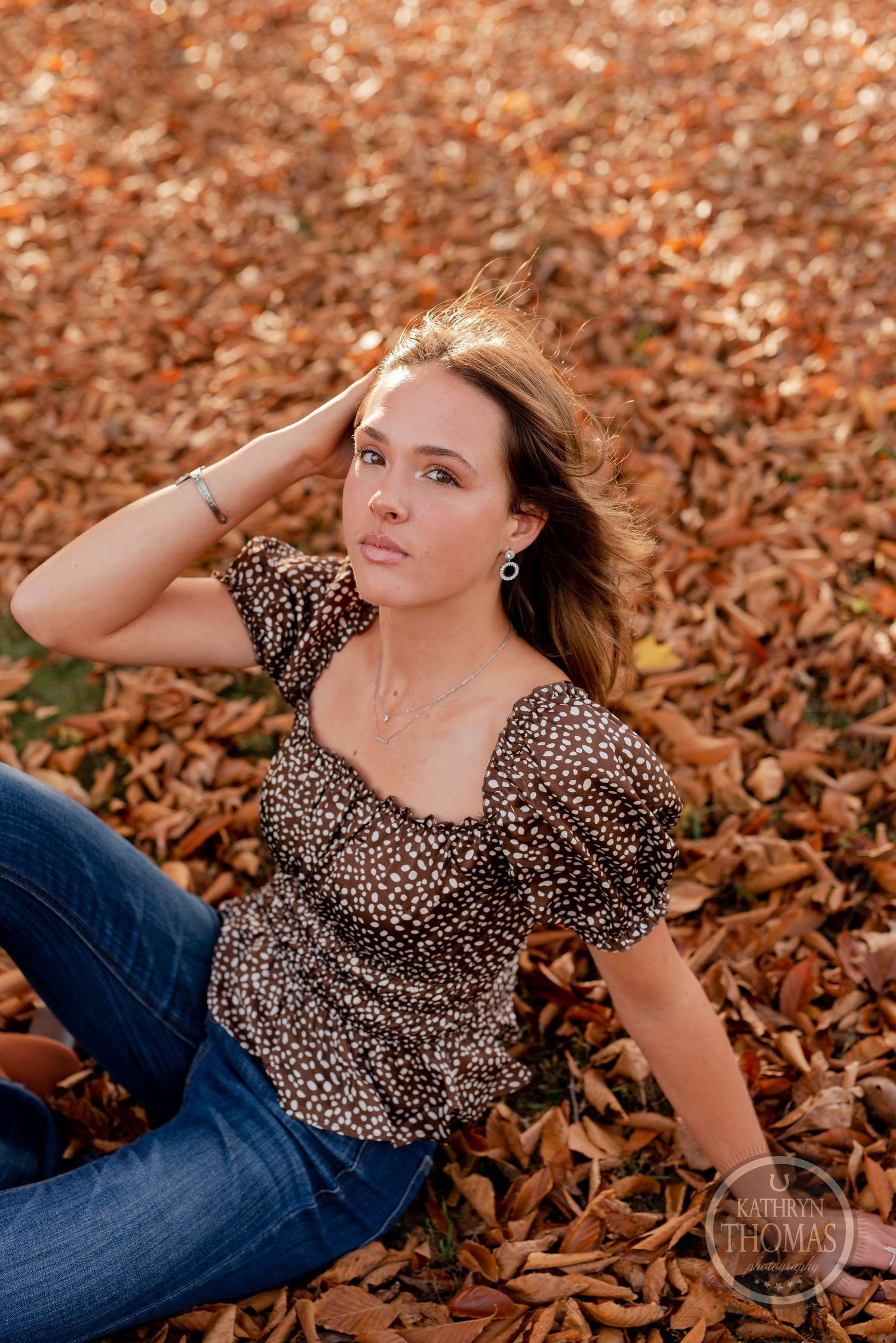 Autumn portrait with wind-blown hair wearing leopard print top and jeans among fallen leaves.