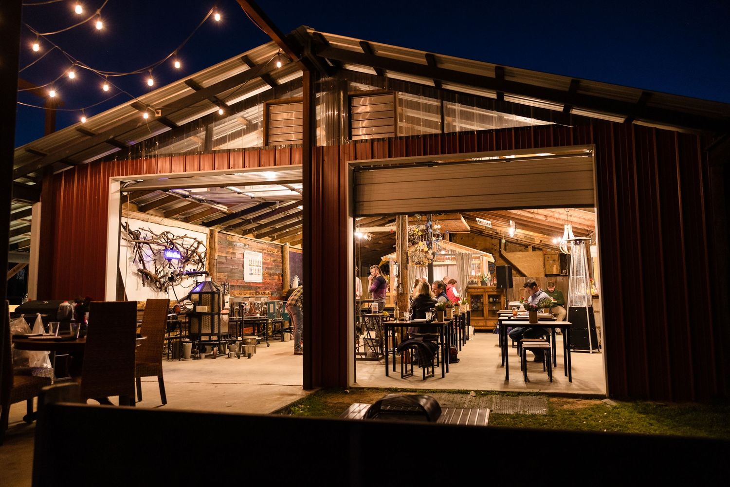 Rustic barn venue at night with warm lighting and outdoor seating visible through large windows.