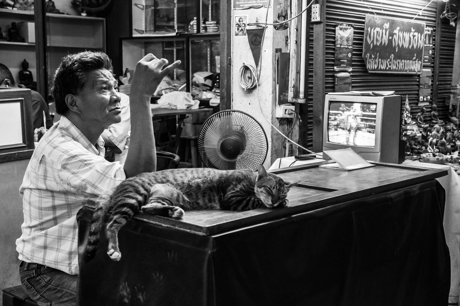 Black and white photo of a small shop interior with vintage electronics and a fan on a desk.