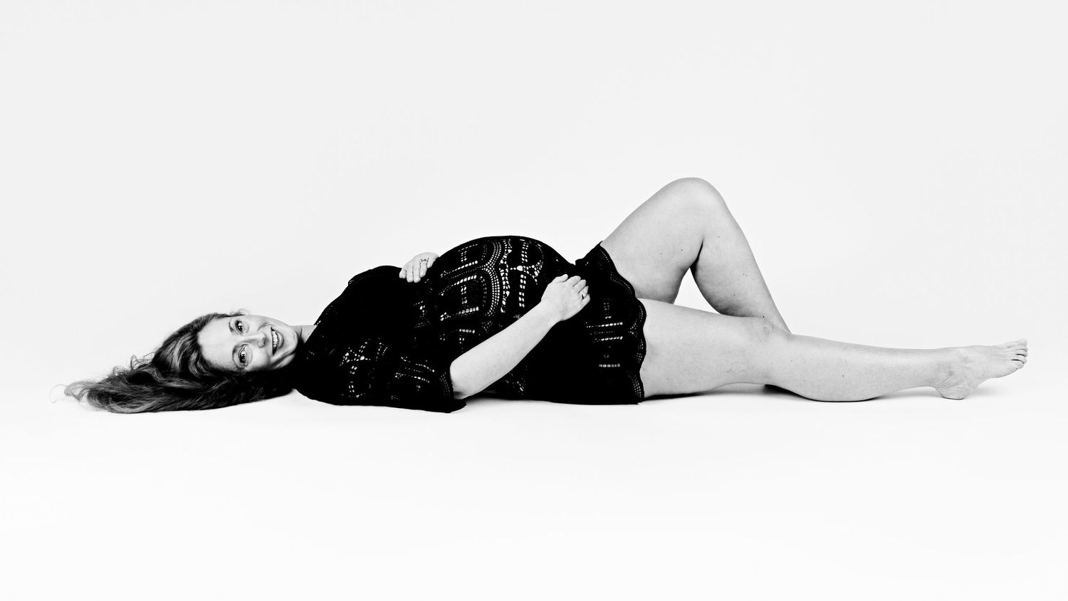 Black and white photo of pregnant woman lying on floor in dark lace dress.