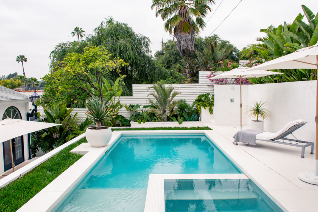 Modern backyard with sleek swimming pool, palm trees and white exterior architecture.