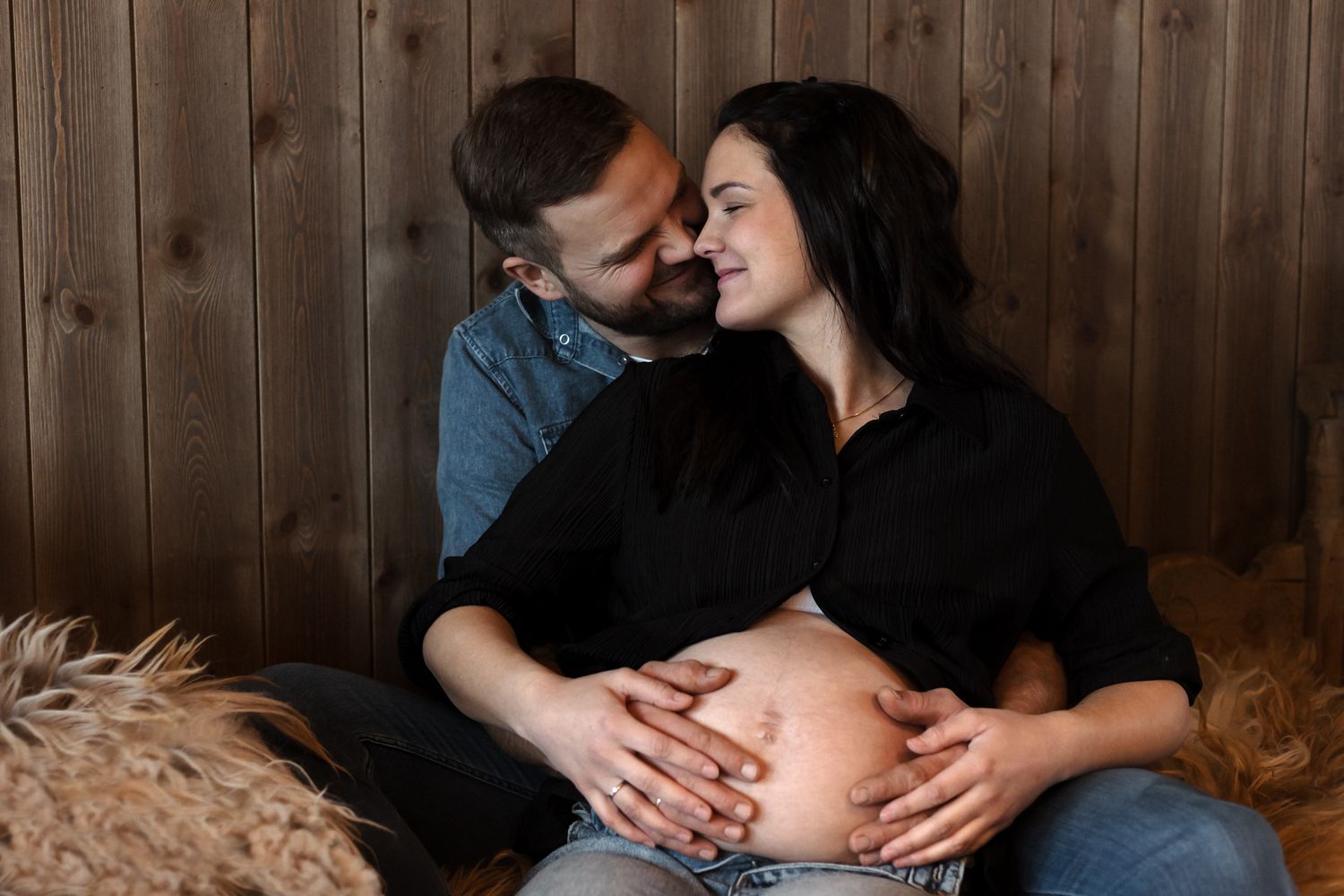 A romantic maternity photo session shows intimate moments between a couple in a rustic barn setting.