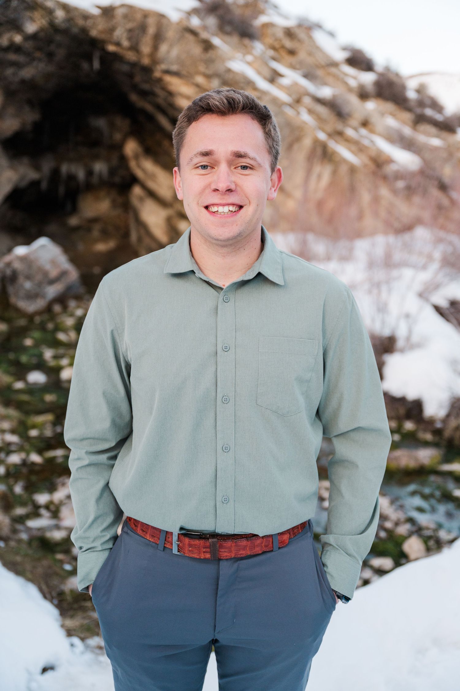 A man in a sage green shirt poses against a snowy mountain landscape.