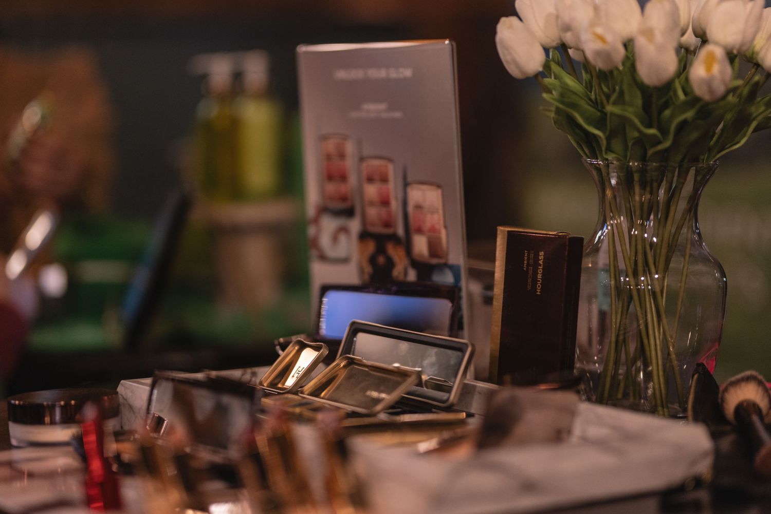 Close-up of makeup products and accessories with white flowers in a vase.