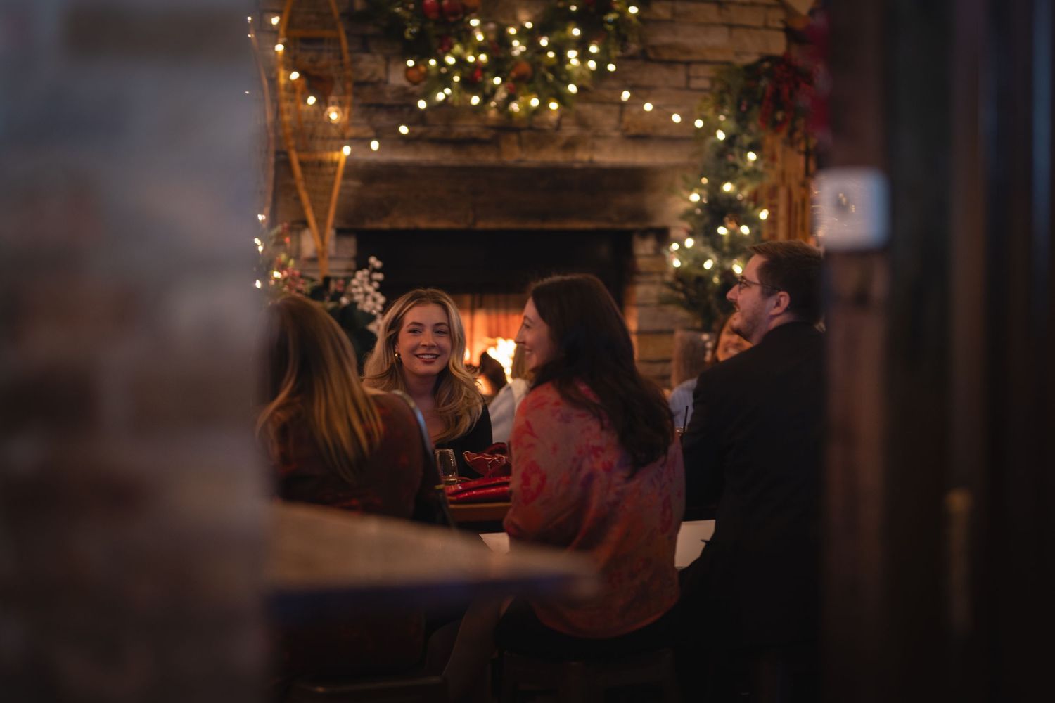 Group enjoying conversation in a cozy room with Christmas lights and fireplace.