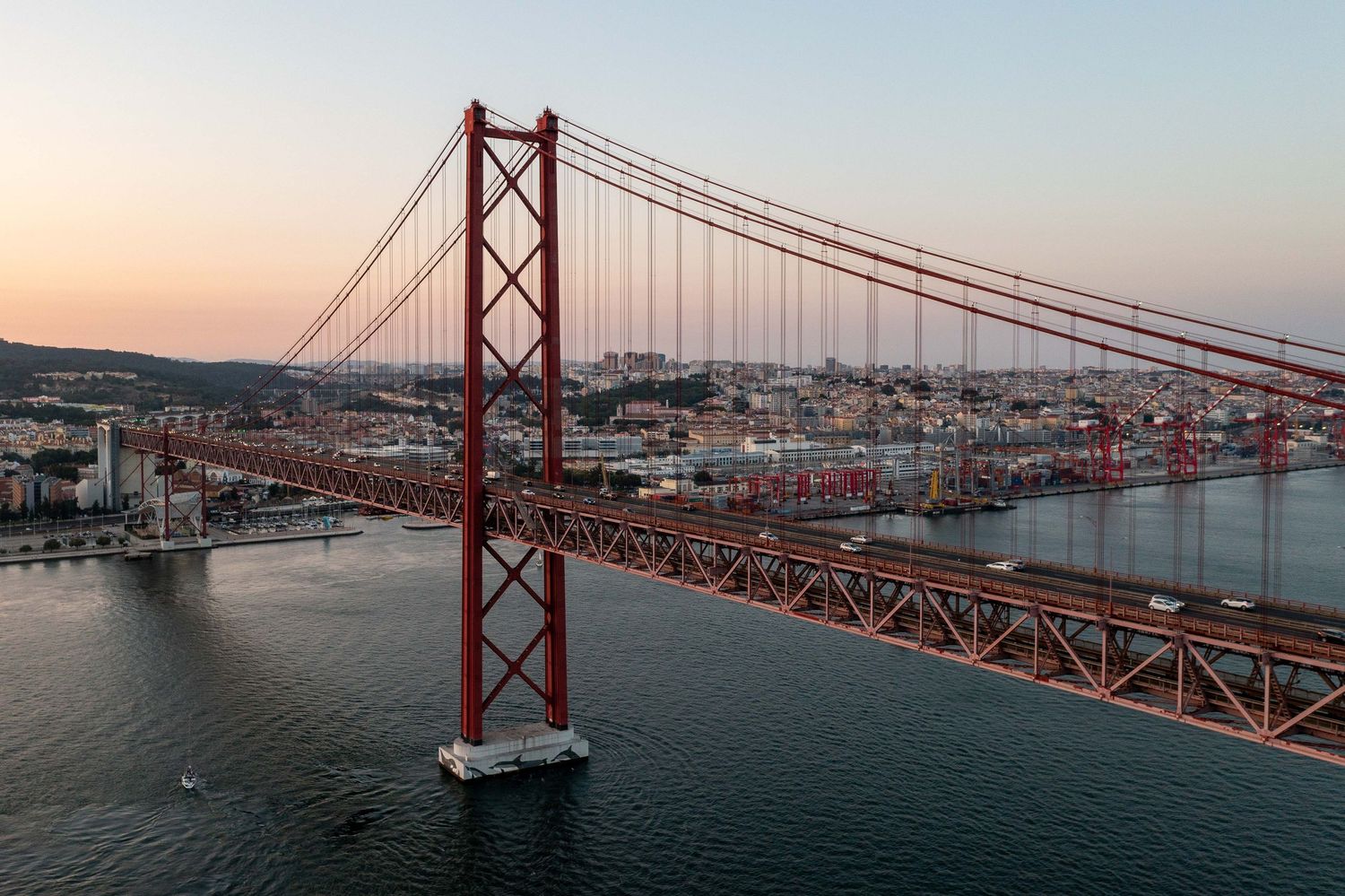 Iconic 25 de Abril Bridge spans across Tagus River in Lisbon at sunset.