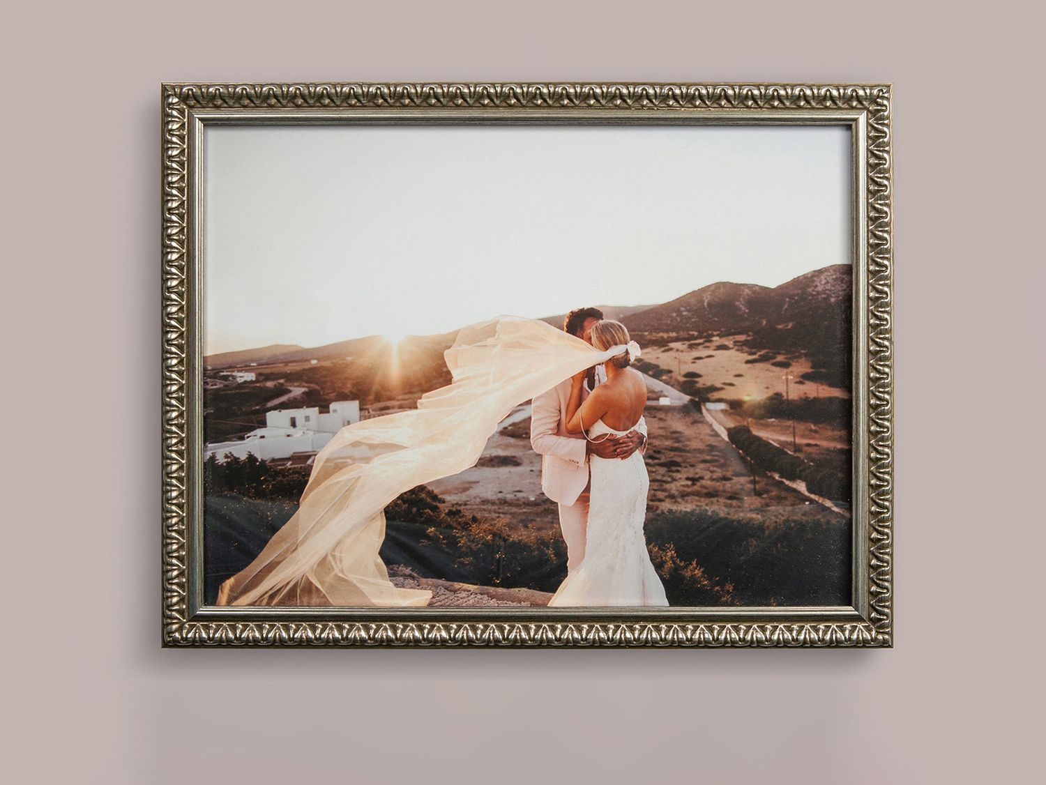 A framed wedding photo capturing a romantic sunset moment with flowing veil against a mountainous landscape.