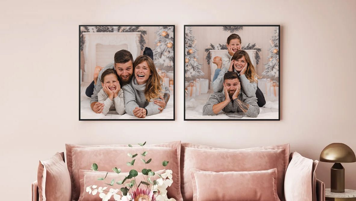 Two large framed family photos hanging above pink velvet couch with decorative pillows.