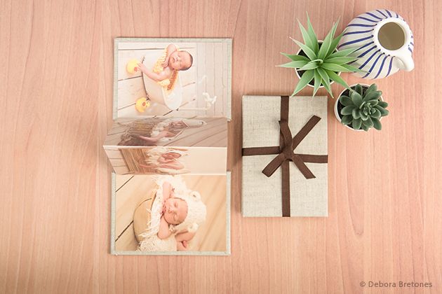 Flat lay of photo prints with wrapped gift box and decorative plants on wooden surface.