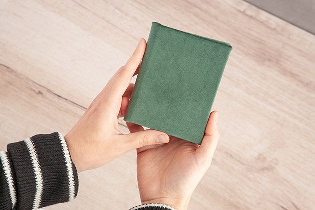 Hands holding small green photo album against wooden background.