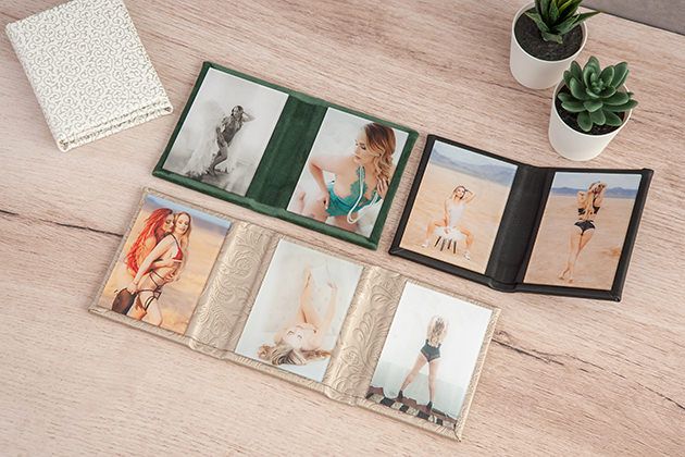 Collection of wedding photo prints displayed in green and beige folios on wooden surface.
