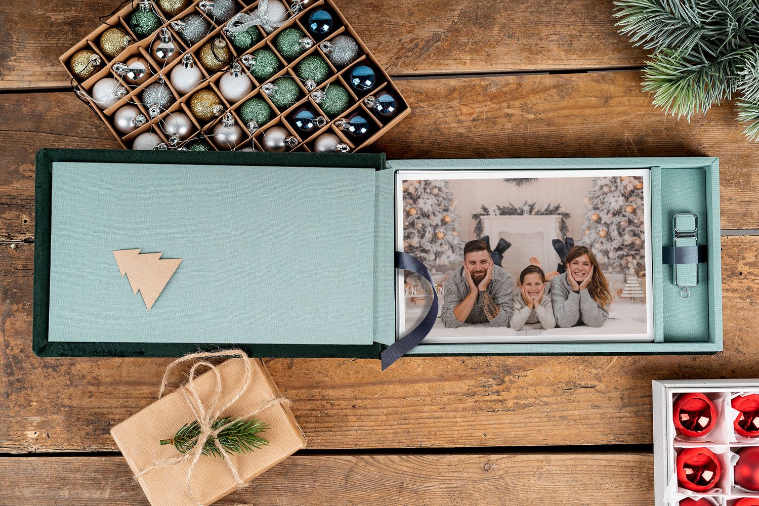 Teal photo album box with decorative chocolates and wrapped gift on wooden table.