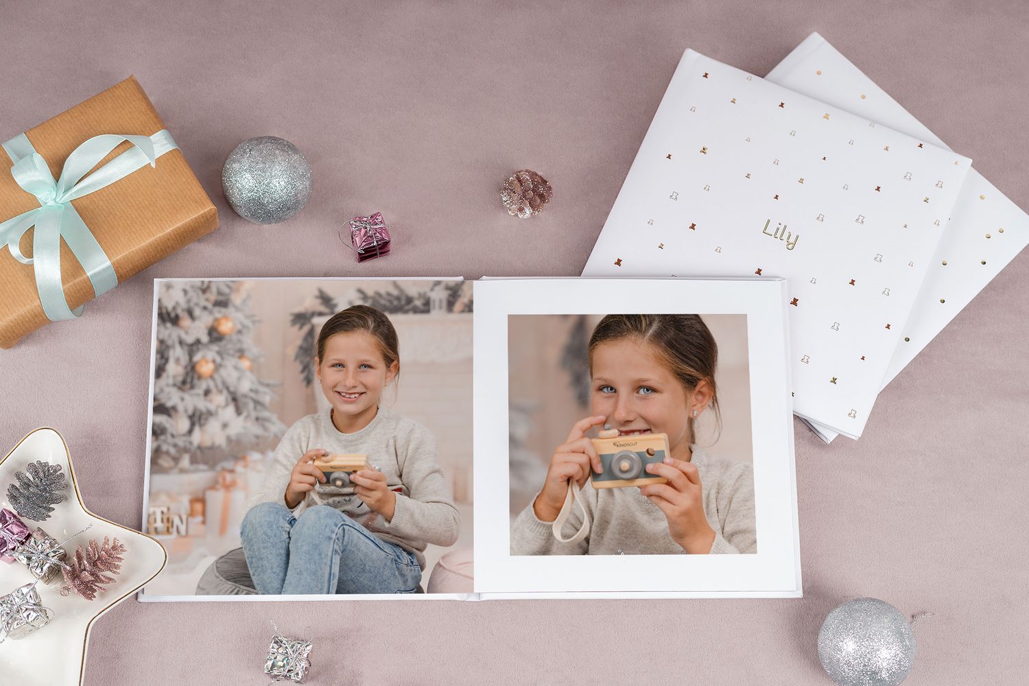 Holiday themed photo prints displayed with festive decorations and silver ornaments on pink background.