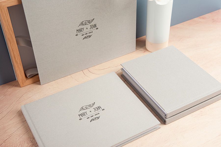 Two elegant gray photo albums with custom logo designs on wooden surface.
