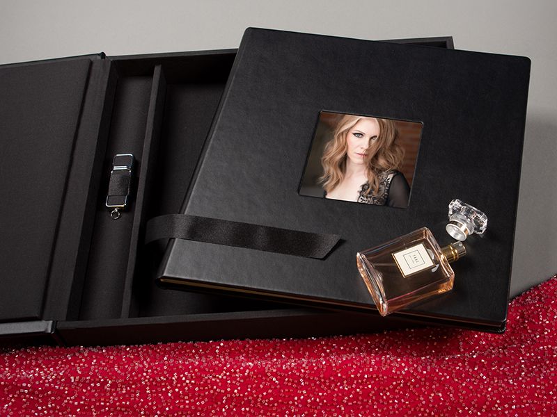 Luxury black photo album with perfume bottle and photograph displayed on red glitter surface.