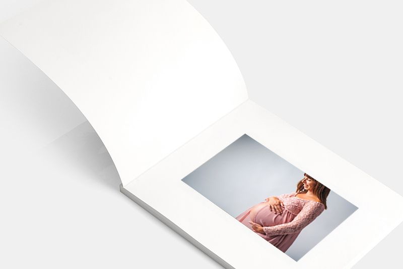 Open white photo album showing maternity portrait on right page.