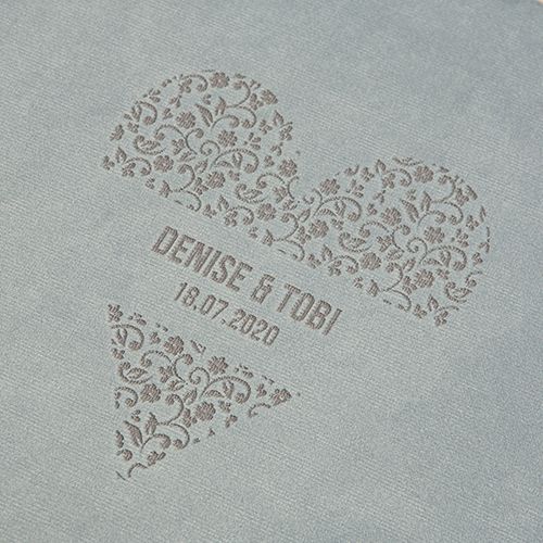 Decorative heart pattern with names and date embossed on light gray textured surface.