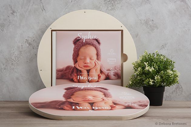 Round photo display with baby portraits and decorative plant on a concrete textured surface.