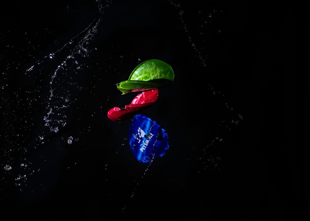 Vibrant red, green, and blue objects with water splashes captured against a dark black background.