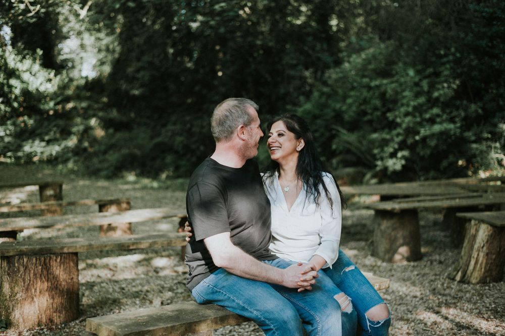 A couple sitting together on a log in a wooded outdoor setting.