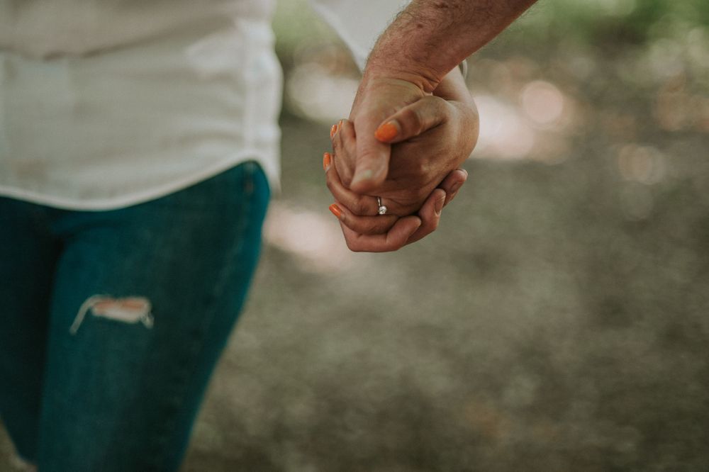 Close-up shot of two hands clasped together in an intimate moment outdoors.