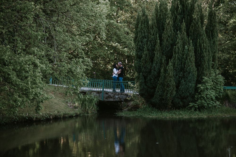 A couple embracing on a blue bridge over calm water surrounded by cypress trees.