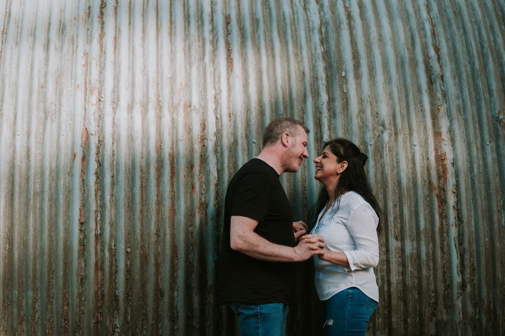 A romantic couple shares an intimate moment against a corrugated metal wall background.