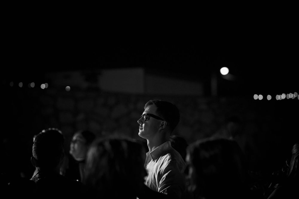 Silhouetted crowd gazing upward at a nighttime event with bokeh lights in the background.