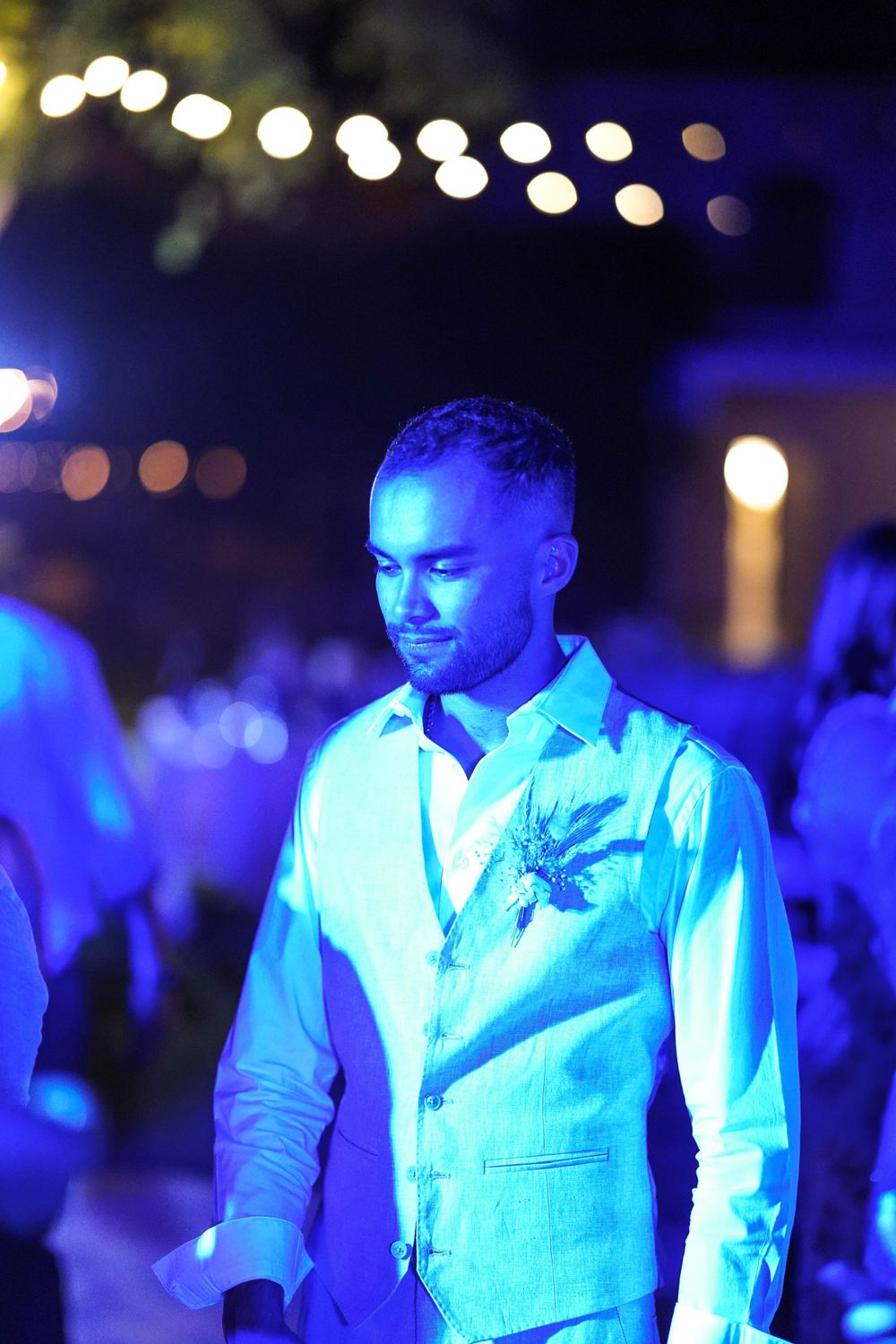 Groomsmen illuminated by blue lighting at a nighttime wedding celebration.