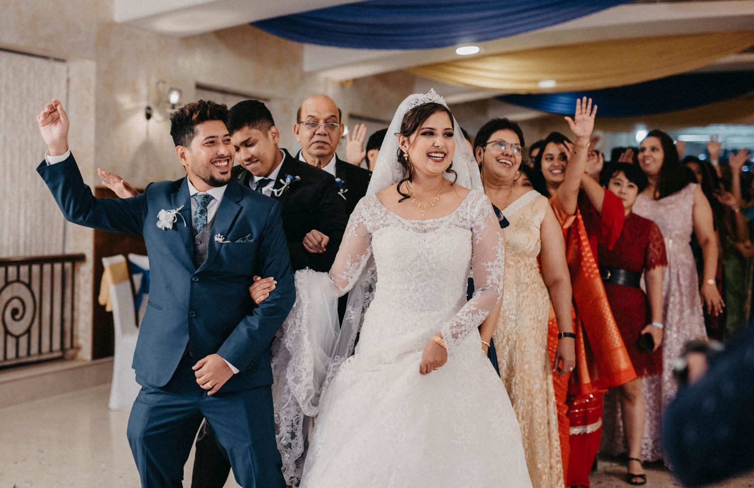 Wedding reception venue decorated with blue draping and filled with celebrating guests.