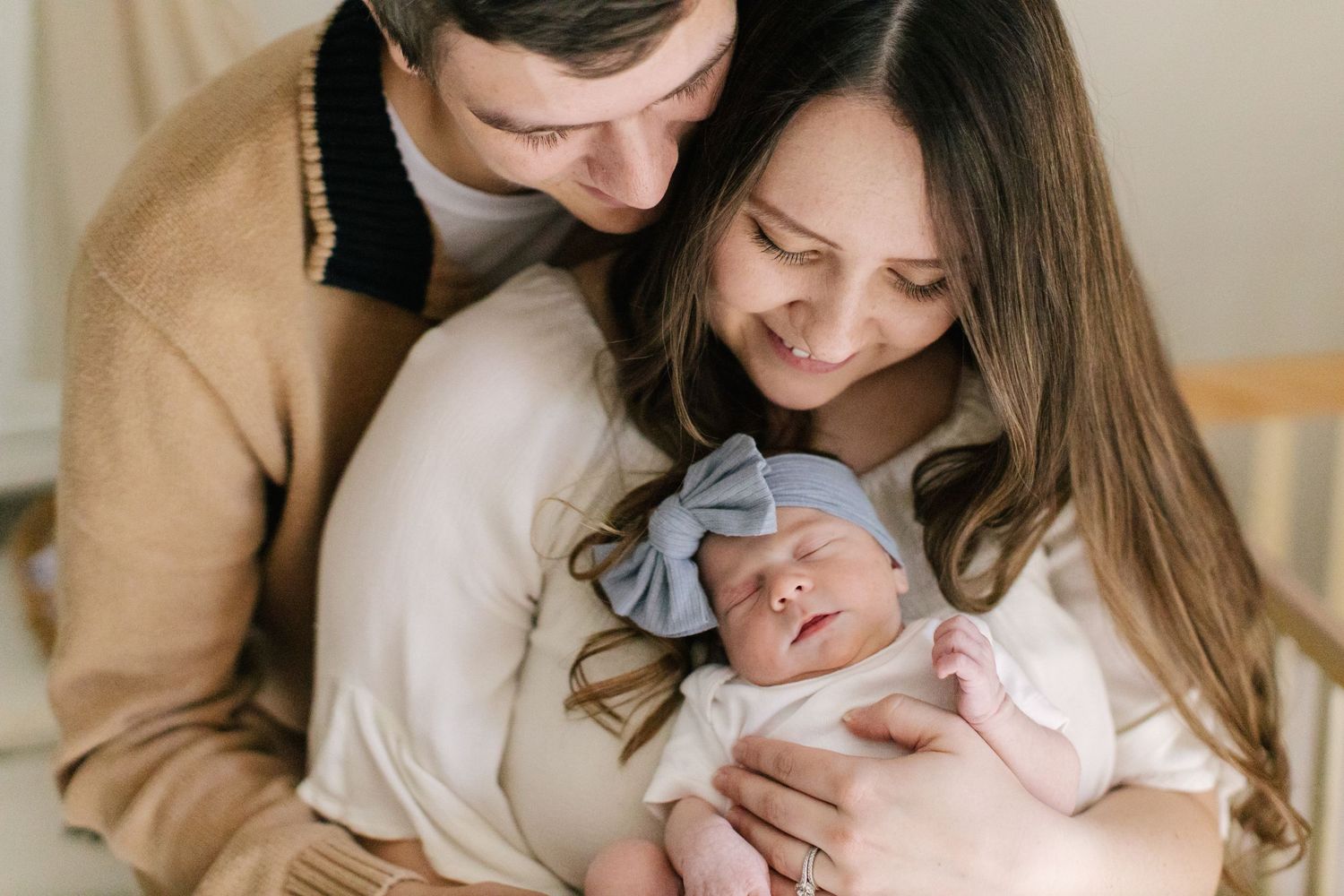 Family snuggling with sleeping newborn baby in cozy home setting.