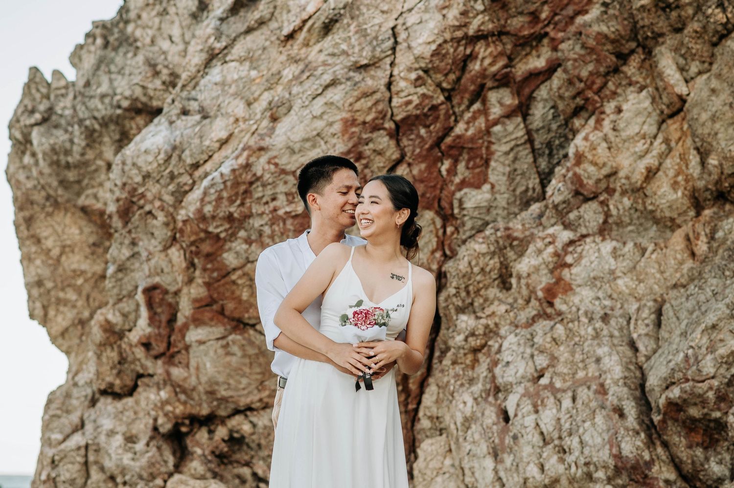 Romantic couple embracing against dramatic rocky cliff backdrop.