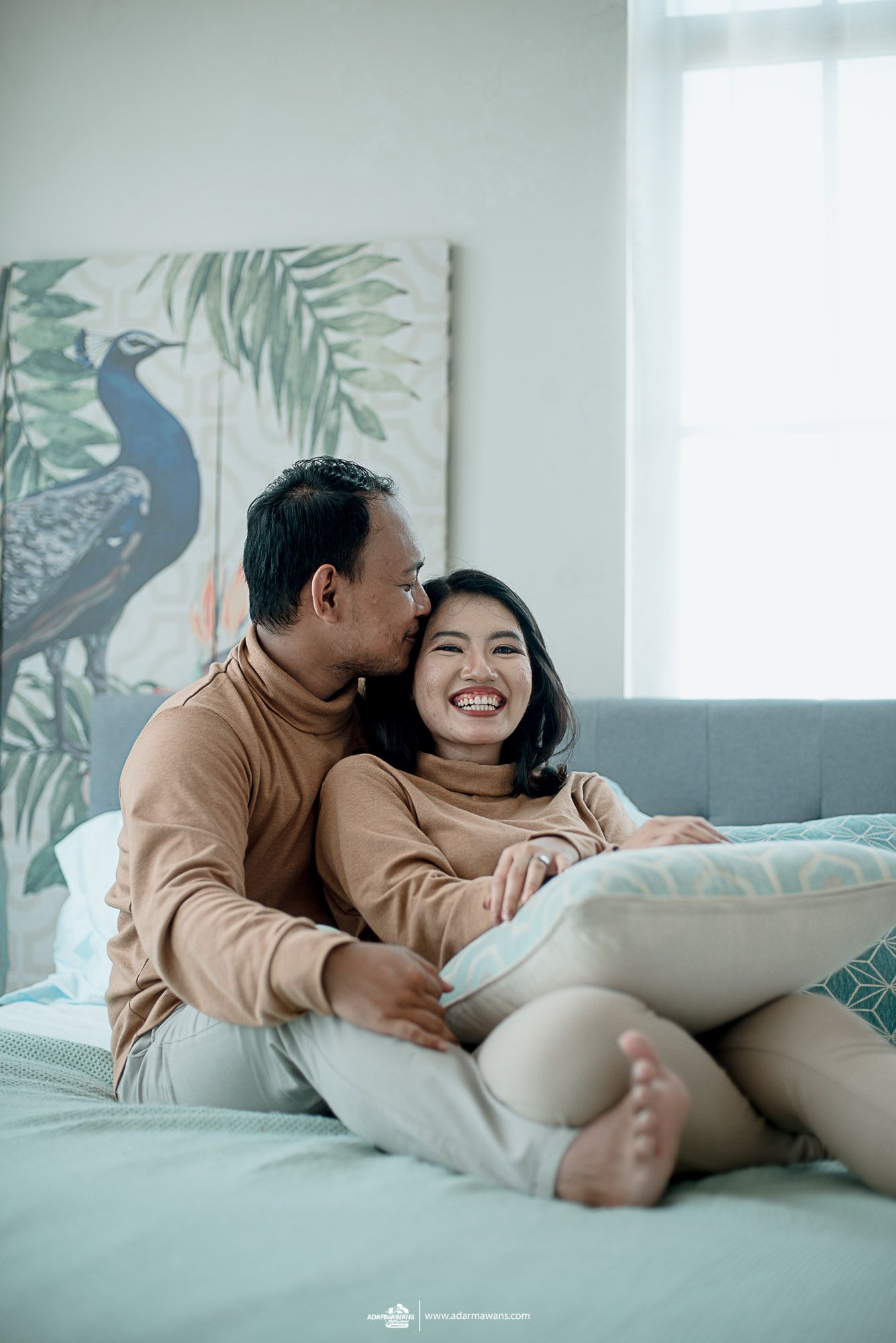 A couple shares a joyful moment on a couch with tropical decor in the background.