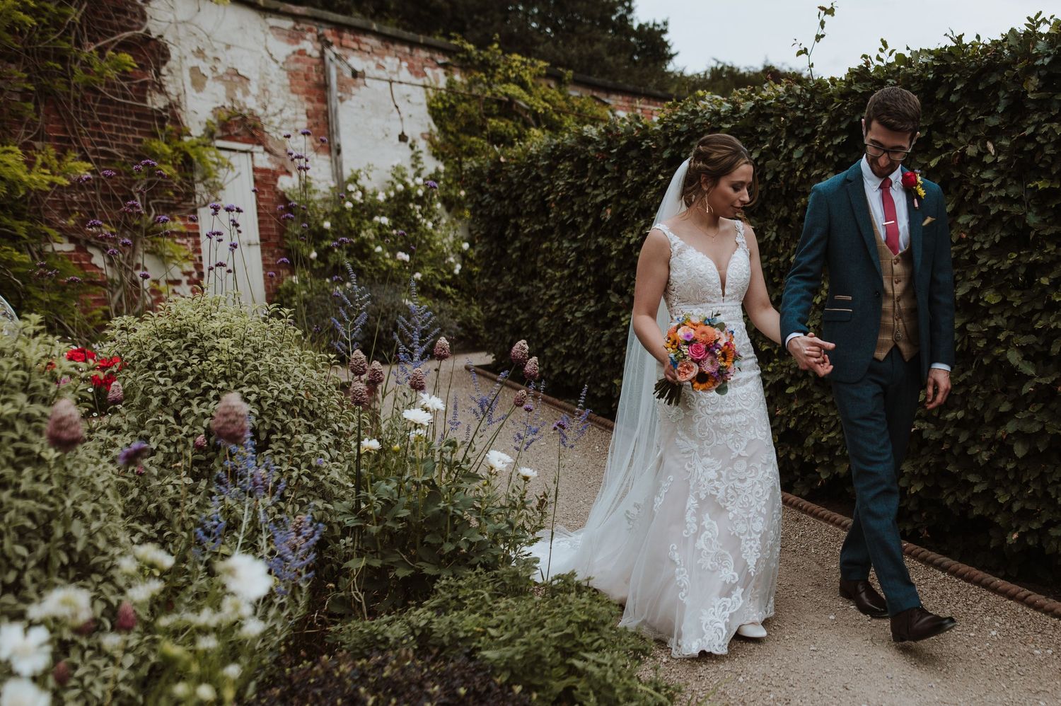 Couple walking through lush garden path after wedding ceremony.
