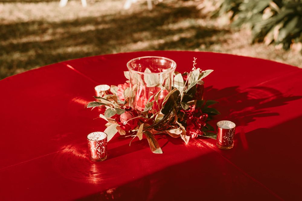 A floral centerpiece with red and pink flowers on a bright red tablecloth outdoors.