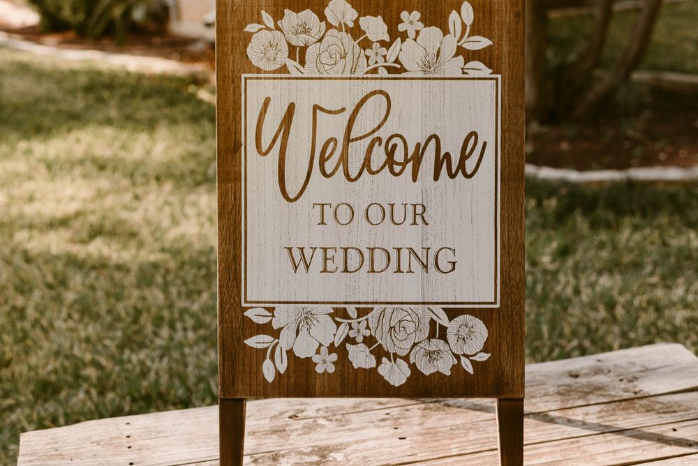 Wooden wedding welcome sign with floral details displayed outdoors.